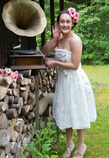 Moderne und trägerlose Brautdirndl aus Jacquard mit Schürze aus Spitze.